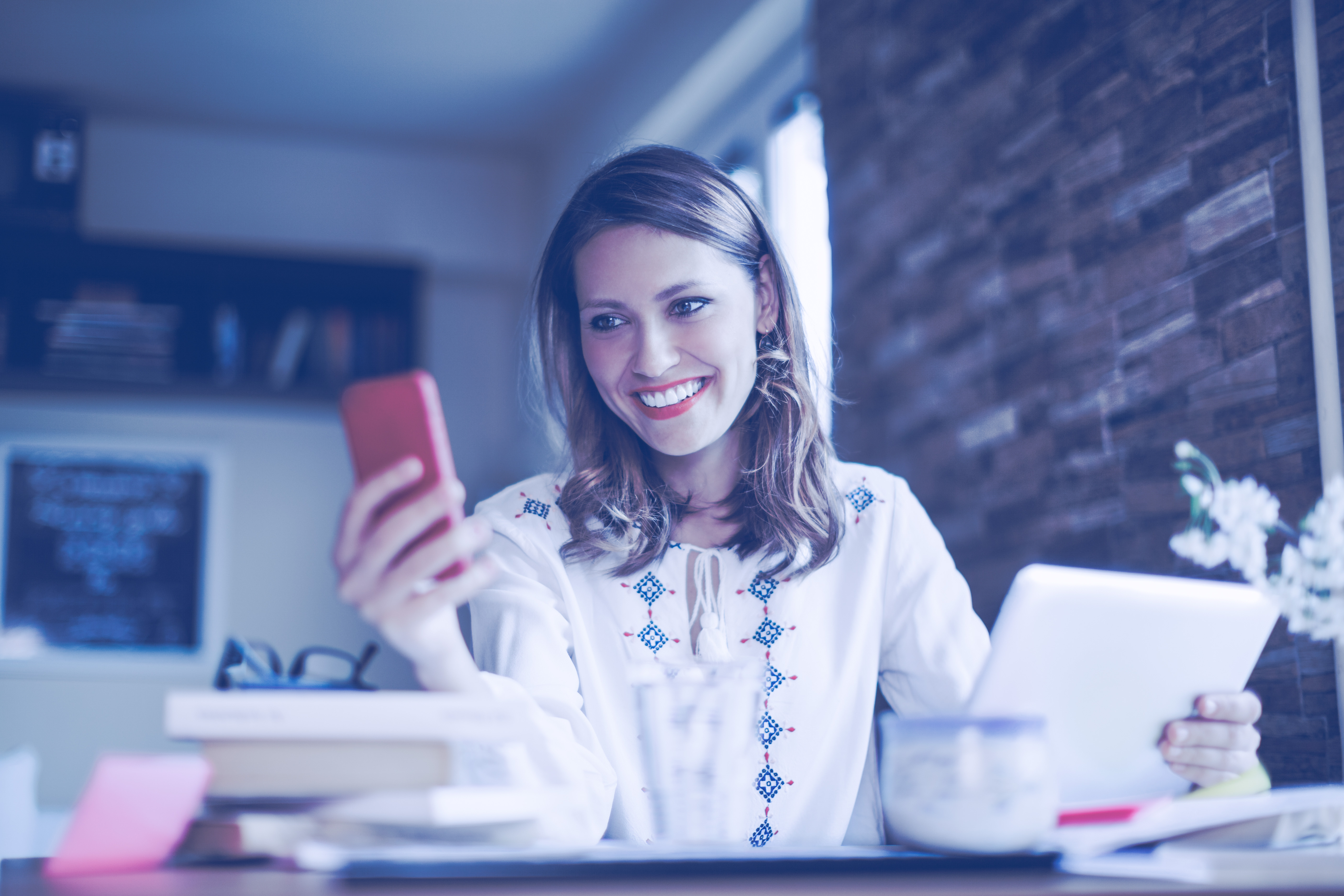 Automatización de las cuentas a pagar - Mujer bonita trabajando desde el hogar; está revisando su teléfono móvil en una mano y sosteniendo su tablet digital en la otra mano